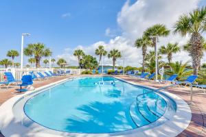a large swimming pool with blue chairs and palm trees at Emerald Dreams Lakefront PCB Vacation Rental! in Panama City Beach
