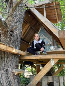 Une jeune fille assise dans une cabane dans les arbres dans l'établissement Casă din povești în mijlocul naturii!, à Arad