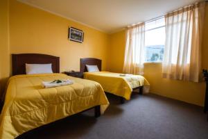 2 camas en una habitación con paredes amarillas y ventana en La Posada de Lucero, en Chivay