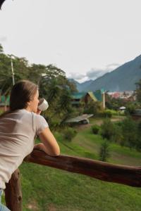 a woman leaning on a wooden fence drinking a drink at Cabañas Palma Sky Lodge in Oxapampa