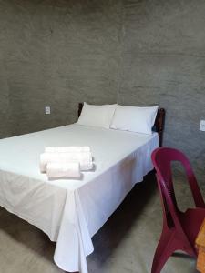 a bed with white sheets and a red chair at Chalé Rj Rio in Santo Amaro