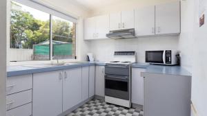 a kitchen with white cabinets and a sink and a microwave at Beachcomber in Old Bar