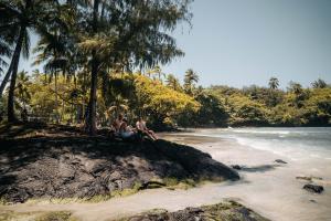 dos hombres sentados en una roca en la playa en Howzit Hostels Hawaii, en Hilo