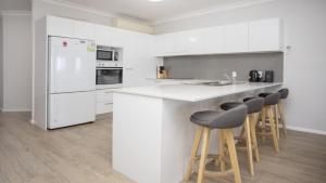 a kitchen with white cabinets and a counter with stools at Apartment 14 - The Meridian in Old Bar