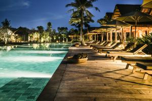 a resort pool with benches and umbrellas at night at Zannier Hotels Phum Baitang in Siem Reap