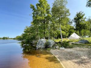 a tent next to a lake with trees and rocks at Urshult Glamping in Urshult