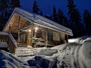 una cabaña de madera en la nieve por la noche en Cottage by the Muonio river for 6 person en Kolari