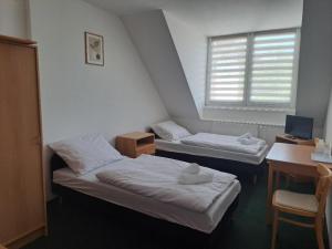 two beds in a room with a desk and a window at Penzion Škubánek in Mladá Boleslav