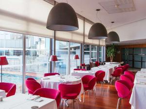 ビアリッツにあるソフィテル ビアリッツ レ ミラマー タラッサの白いテーブルと赤い椅子、窓のあるレストラン