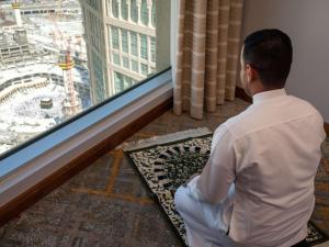 Un uomo seduto sul pavimento che guarda fuori da una finestra di Swissotel Al Maqam Makkah a La Mecca