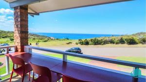 a balcony with a table and chairs and a car on the road at Oceanview Beach House in Caves Beach