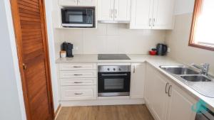 a kitchen with white cabinets and a sink and a microwave at Ripples by the Sea in Caves Beach