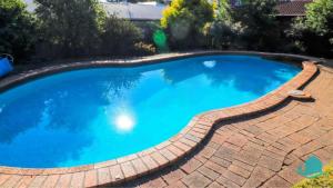 a large blue swimming pool with a brick pathway around it at Wemberley Lakehouse in Wangi Wangi