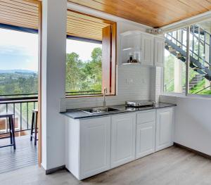 a kitchen with white cabinets and a balcony with windows at Waterfall Villa by Opulence in Talawakele