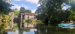 una casa en un río con un barco delante en Moulin de Courcelles en Aubréville