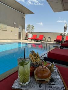 uma bandeja com uma sanduíche e uma bebida junto a uma piscina em Centro Al Manhal by Rotana em Abu Dhabi