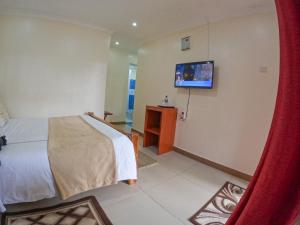 1 dormitorio con 1 cama y TV en la pared en Mayas Suites en Nyeri