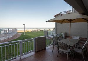 einen Balkon mit einem Tisch mit Stühlen und einem Sonnenschirm in der Unterkunft Jeffreys Bay Villas on The Beach in Jeffreys Bay