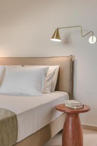 un letto con lenzuola bianche e un tavolo con una lampada di Rodi Studios a Karavádhos