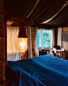 a bedroom with a blue bed and a window at DugDug Camps - Glamping Amidst Nature in Bhīm Tāl