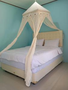 - une chambre dotée d'un lit à baldaquin avec des draps et des oreillers blancs dans l'établissement RIUNG LALONG TERONG Guest House, à Riung