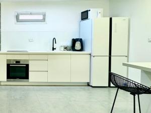 a white kitchen with a refrigerator and a chair at מיני דירת פנטהאוז in Rishon LeẔiyyon