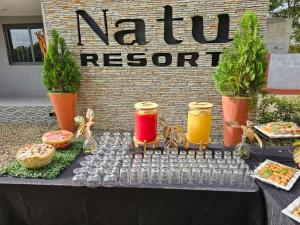 Natu Resort的一张桌子上摆放着饮料和食物，旁边立着一块牌子