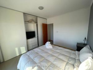 um quarto com uma cama branca e uma televisão em Departamentos Leloir em Neuquén