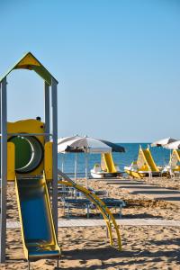 un parco giochi su una spiaggia con sedie e ombrelloni di Aparthotel Pineda a Bibione
