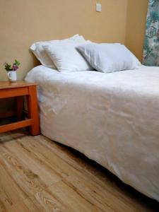 a bed with white sheets and pillows next to a table at The Orange Cottage in Nyeri