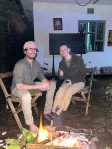two men sitting on chairs next to a fire at Meleji studio room in Arusha