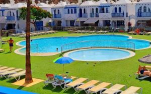 a large swimming pool with chairs and an umbrella at Pool Front Playmar Maspalomas in San Bartolomé