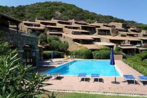 a resort with a swimming pool in front of a mountain at By the sea with amazing view in Capo Coda Cavallo