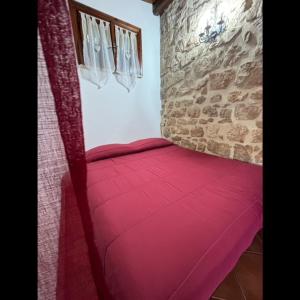 Una cama roja en una habitación con una pared de piedra. en Summer House en Fondi