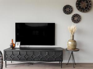 a black entertainment center with a tv on a white wall at Nature Escape w Sauna in Wissenkerke