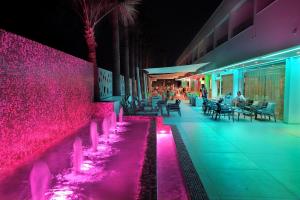 a resort with a pink wall and tables and chairs at Nelia Beach Hotel & Spa in Ayia Napa
