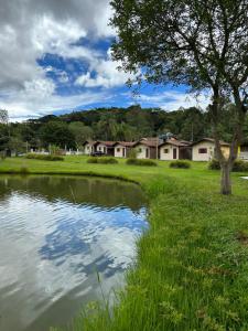 un étang dans un champ avec des maisons en arrière-plan dans l'établissement Chácara Kamaleão, à Córrego do Bom Jesus