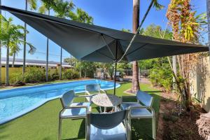 a table and chairs with an umbrella next to a swimming pool at Paravista Motel in Darwin
