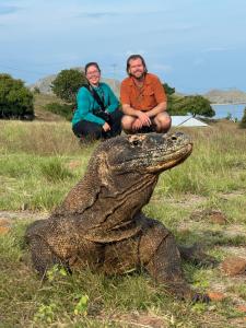 dos personas sentadas junto a un cocodrilo en un campo en Jhuna Komodo Homestay, en Komodo