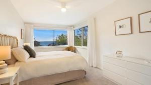 a white bedroom with a bed and a window at 'Surfside' by HolidayCo in Killcare