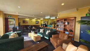 una sala de estar con sofás y sillas y una biblioteca. en Franz Josef Montrose Lodge en Franz Josef