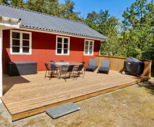 une terrasse en bois avec une table, des chaises et une télévision. dans l'établissement Charming Cottage Close To The Beach, à Vester Sømarken