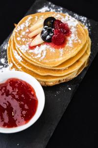 a stack of pancakes with berries and a bowl of sauce at Casa Art Ubud in Ubud