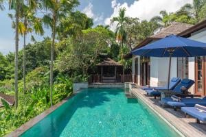 a swimming pool with chairs and an umbrella next to a house at Villa Umah Raja in Lovina