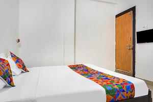 プネにあるFabHotel Galaxy Airport Innの白いベッド1台、木製のドアが備わるベッドルーム1室が備わります。