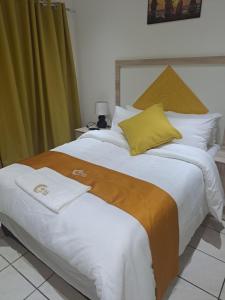 uma cama grande com lençóis brancos e almofadas amarelas em Akyra Guest House Brackenhurst em Alberton
