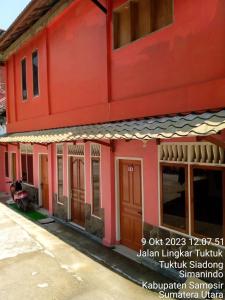 a red building with wooden doors on a street at Thenewgoldensunrise in Tuktuk Siadong