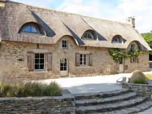 a large stone building with a roof with a stone staircase at Maison typique bretonne avec toit de chaume in Camors