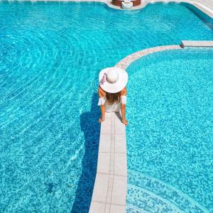 a little girl in a hat standing next to a swimming pool at Hotel Luxor in Milano Marittima