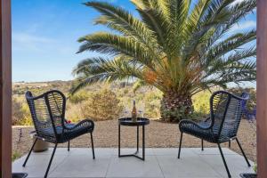 two chairs and a table in front of a palm tree at Hill Moi Country stay by the Sea in Victor Harbor